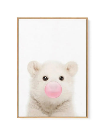 Framed canvas art print featuring a young white polar bear against a white background, blowing a large bubble gum bubble in soft pink. The bear has dark eyes and rounded ears, rendered in soft, naturalistic tones. The artwork is displayed in a natural wood frame with a white border, creating a minimalist, whimsical composition suitable for nurseries or contemporary spaces.