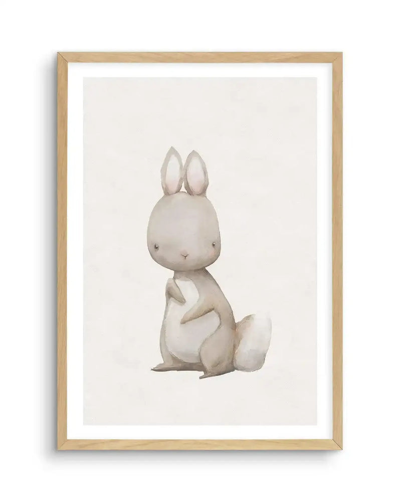 Watercolour art print featuring a cute, plump bunny with large ears and a small, fluffy white tail, rendered in soft grey and cream tones on a light cream background, displayed in a natural oak frame with white border.