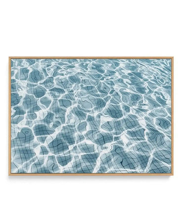 Framed canvas art print featuring an overhead view of a swimming pool with blue tile floor visible beneath clear, rippling water. White light reflections create organic, wavy patterns across the water's surface. The composition uses a serene palette of teal, slate blue, and white. The canvas is mounted in a natural wood frame with a white border.