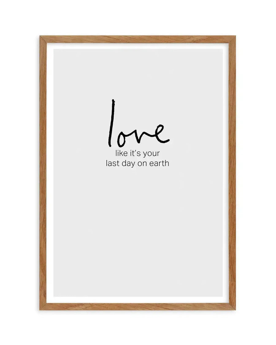 Framed art print with natural wood frame and white border featuring black handwritten-style text on a light gray background. The word "love" appears in larger, cursive script in the upper portion, with the phrase "like it's your last day on earth" in smaller, regular font below it. The minimalist design conveys an inspirational message through simple typography and neutral color palette.