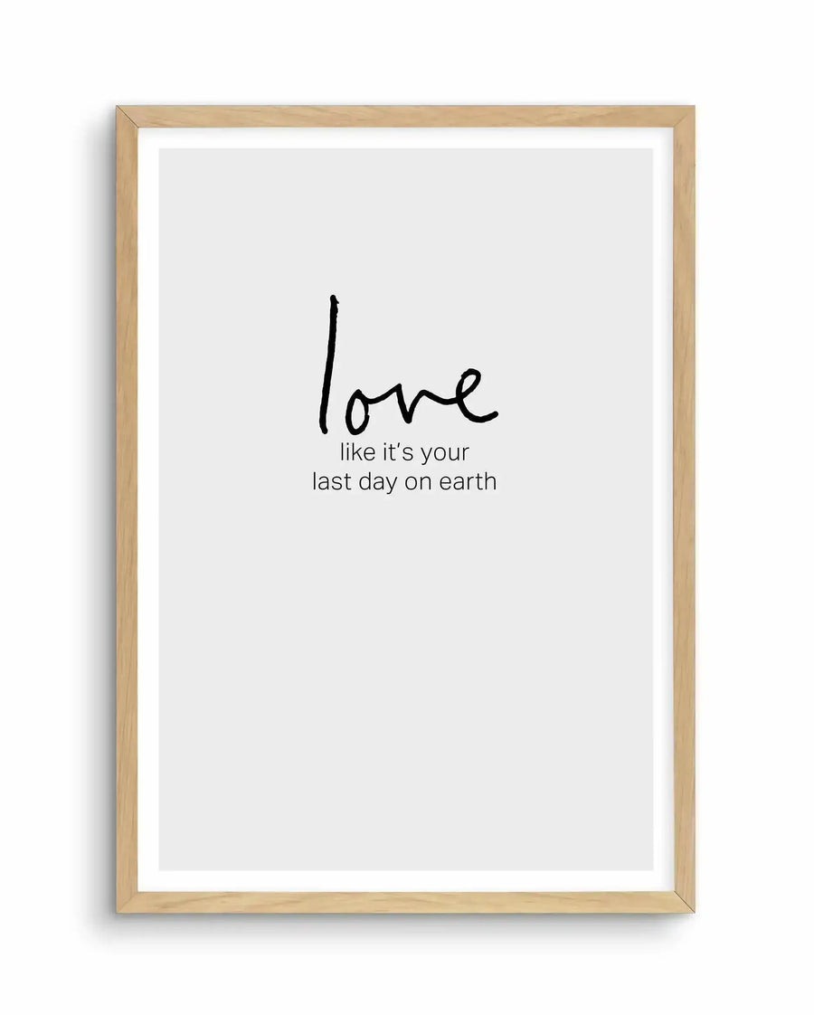 Art print with light wood frame and white border featuring handwritten-style black text on a light gray background. The word "love" appears in larger, casual script at the top, followed by smaller text reading "like it's your last day on earth" positioned below. The minimalist design uses simple black typography centered on the page, conveying an inspirational message with understated elegance.