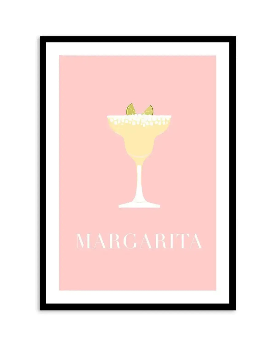 Art print featuring a minimalist illustration of a margarita cocktail in a classic glass with a salted rim and two lime wedges, set against a soft pastel pink background. The drink is a pale yellow-green, and the text "MARGARITA" is printed in white capital letters at the bottom, displayed in a black frame with a white border.