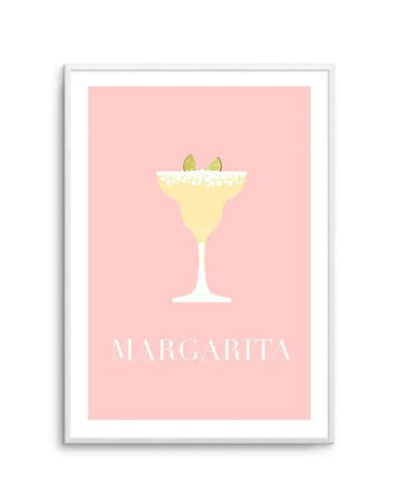 "Minimalist art print featuring a pale yellow margarita cocktail in a classic stemmed glass with a salt-rimmed edge and two lime wedges, set against a solid pastel pink background. The word 'MARGARITA' is printed in white capital letters below the glass. The print is displayed in a white frame with a white border."