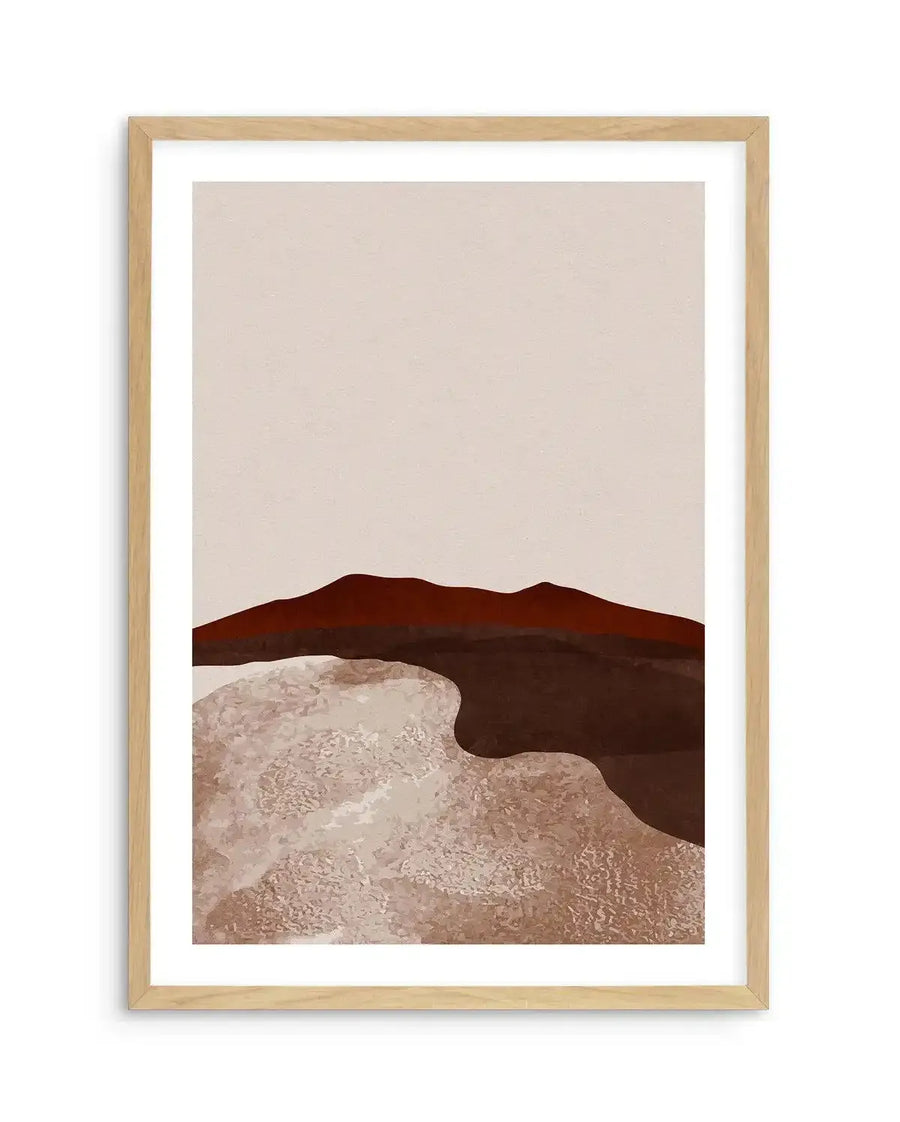 Abstract art print featuring a minimalist desert landscape with a deep reddish-brown mountain range under a pale beige sky. The foreground has textured, undulating shapes in light beige and dark brown, suggestive of sand dunes or a dry riverbed, displayed in a natural oak frame with white border.