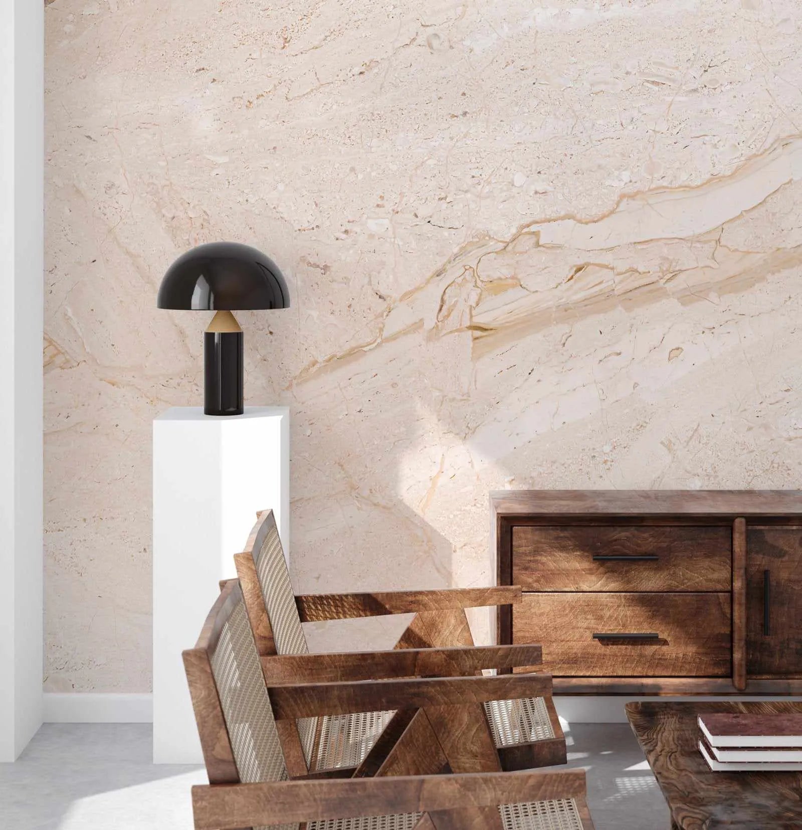 Modern marble wallpaper in blush tones displayed on a feature wall in a minimalist interior. The design features soft cream, dusty rose, and warm tan veining patterns that mimic natural travertine marble with organic flowing lines and subtle texture. The wallpaper is shown in a styled room setting with mid-century modern wooden furniture including a chair with woven details and a wooden sideboard, alongside a black mushroom-shaped table lamp on a white pedestal, creating an elegant, contemporary aesthetic.