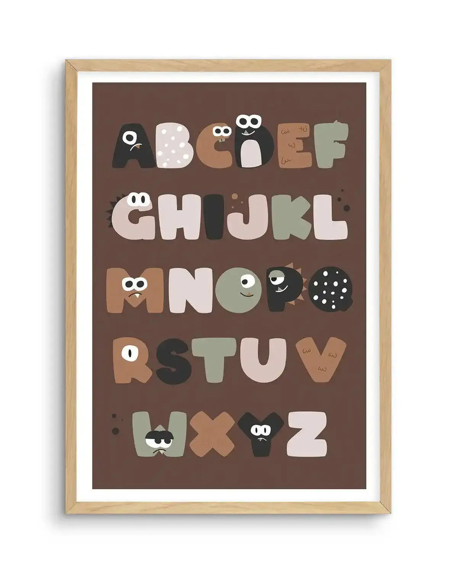 Art print featuring a monster alphabet with each letter depicted as a unique, friendly monster in various shades of brown, beige, grey, and black, displayed in a natural oak frame with white border. The monsters have different expressions, eyes, and textures, creating a playful and whimsical composition.