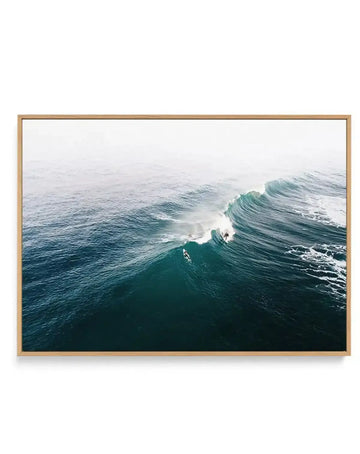 Aerial photograph of turquoise ocean waves at Mornington, Victoria, captured in natural daylight. The composition shows multiple rolling waves with white foam and spray, shot from above with a misty, overcast sky. The water displays deep teal and emerald green tones in the foreground, gradually transitioning to lighter blue-grey in the distance. The image is printed on canvas and displayed in a natural wood frame with a white border.