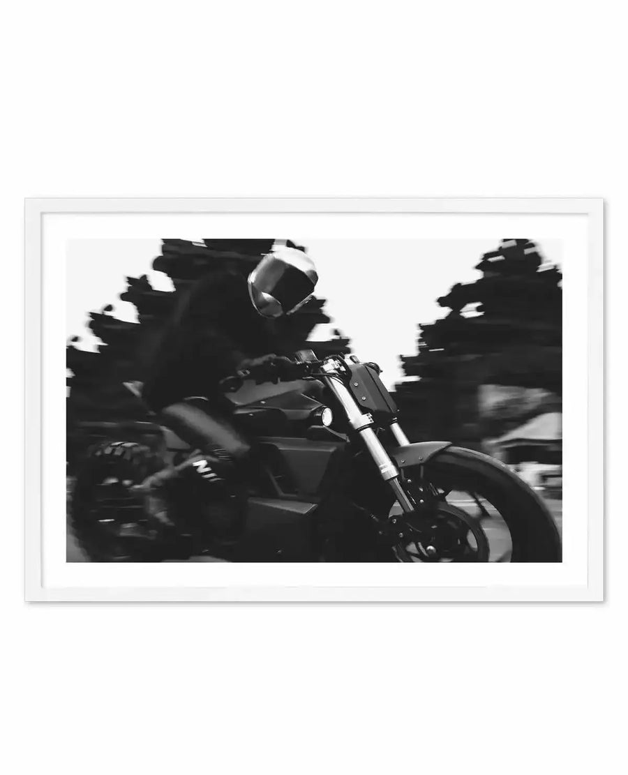 Black and white art print titled "Nice Ride" by Mario Stefanelli, featuring a dynamic motion-blur photograph of a motorcyclist riding a cruiser motorcycle. The rider wears a full-face helmet and leans into the ride, with trees blurred in the background suggesting high speed and movement. The print is mounted in a white frame with a white border, creating stark contrast with the dramatic monochromatic imagery.