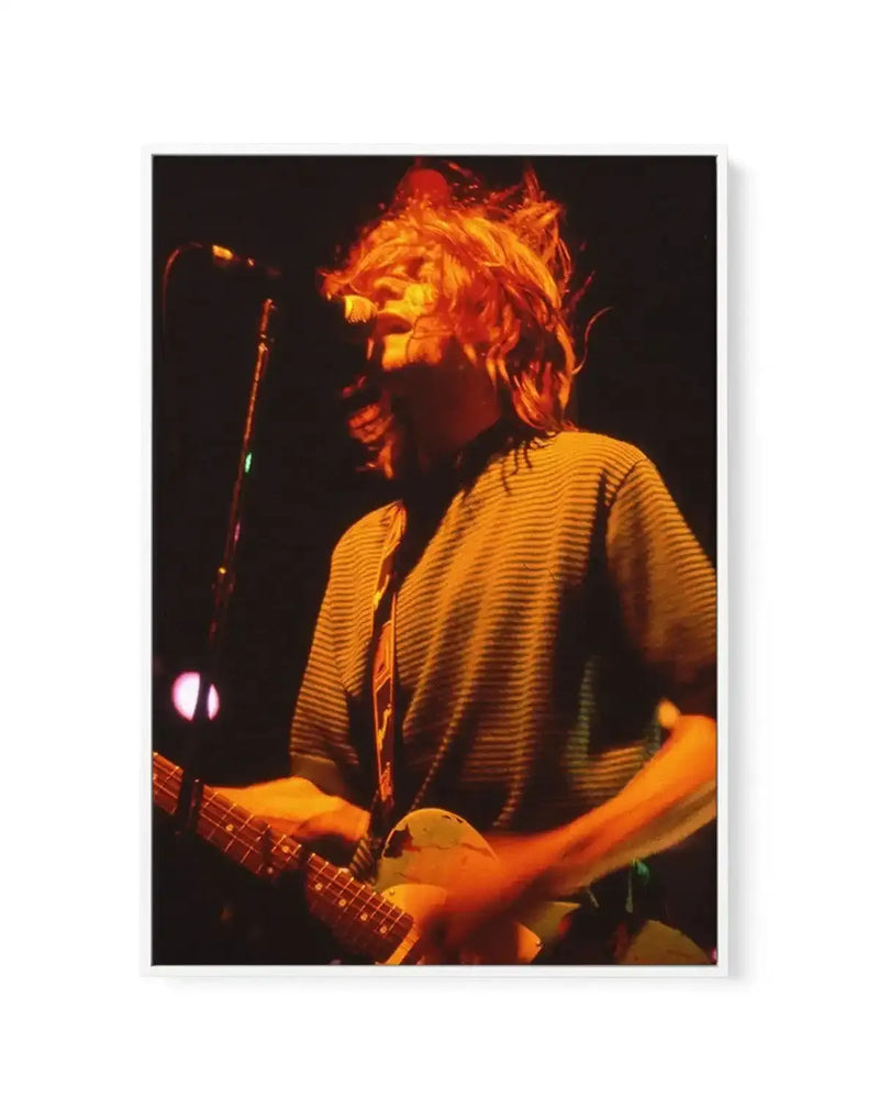 "Gallery-wrapped canvas print of a live performance photograph featuring a male musician with long, messy blonde hair, illuminated by warm orange stage lights, playing an electric guitar. He is wearing a horizontally striped t-shirt and a guitar strap, with a microphone stand visible in the background. The image captures a dynamic moment with motion blur, conveying an energetic mood."