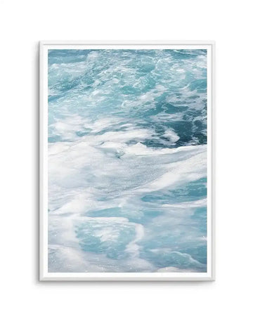Framed art print featuring a photograph of ocean waves and sandy beach. The composition shows turquoise and teal waves with white foamy crests in the upper portion, transitioning to wet sand with gentle waves lapping at the shore in the foreground. The palette includes soft whites, pale aqua, and deeper ocean blue-greens, creating a serene coastal scene. The photograph has a soft, natural light quality with visible sparkle on the water. The artwork is displayed in a white wooden frame with a white border.