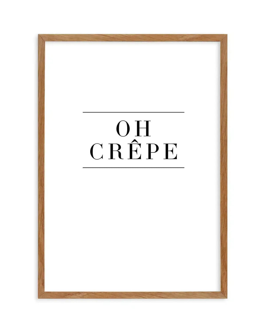 Art print with black serif typography on white background, reading "OH CRÊPE" with decorative horizontal lines above and below the text. The print is displayed in a natural wood frame with a warm honey tone finish.
