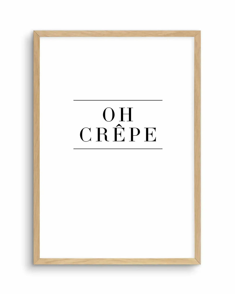 Art print with "OH CRÊPE" in large serif typography, centered on white background with horizontal lines above and below text. Natural wood frame with light tan finish surrounds the print.