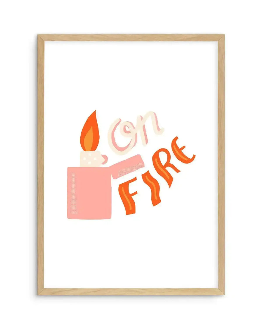 Art print featuring a stylized illustration of a lit pink lighter with a bright orange and yellow flame, next to the hand-lettered words "On Fire" in a playful, wavy font with shades of pale pink and orange, displayed in a natural oak frame with white border.