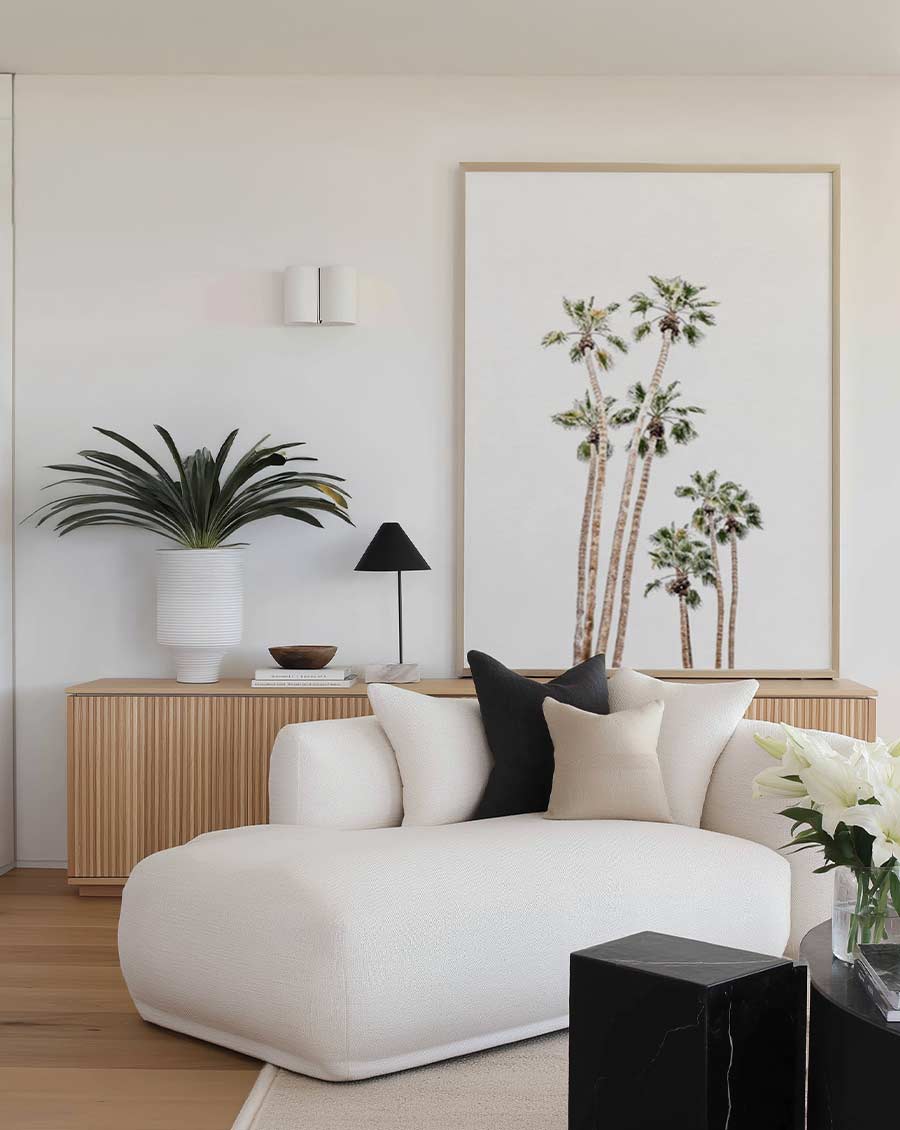 Modern living room with a white sofa, decorative pillows, and a large framed art print of palm trees.