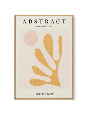 Framed canvas art print titled "Abstract Papiers Découpés Exhibition 2021" featuring minimalist cut-paper style artwork. Design shows a golden-yellow organic hand-like or plant form with elongated curved fingers against a pale cream background, with a soft dusty rose circular shape in the upper left. Natural wood frame with white border. Text at top reads "ABSTRACT" with subtitle "PAPIERS DÉCOUPÉS" and exhibition date at bottom. Flat, matte finish with warm, earthy aesthetic.