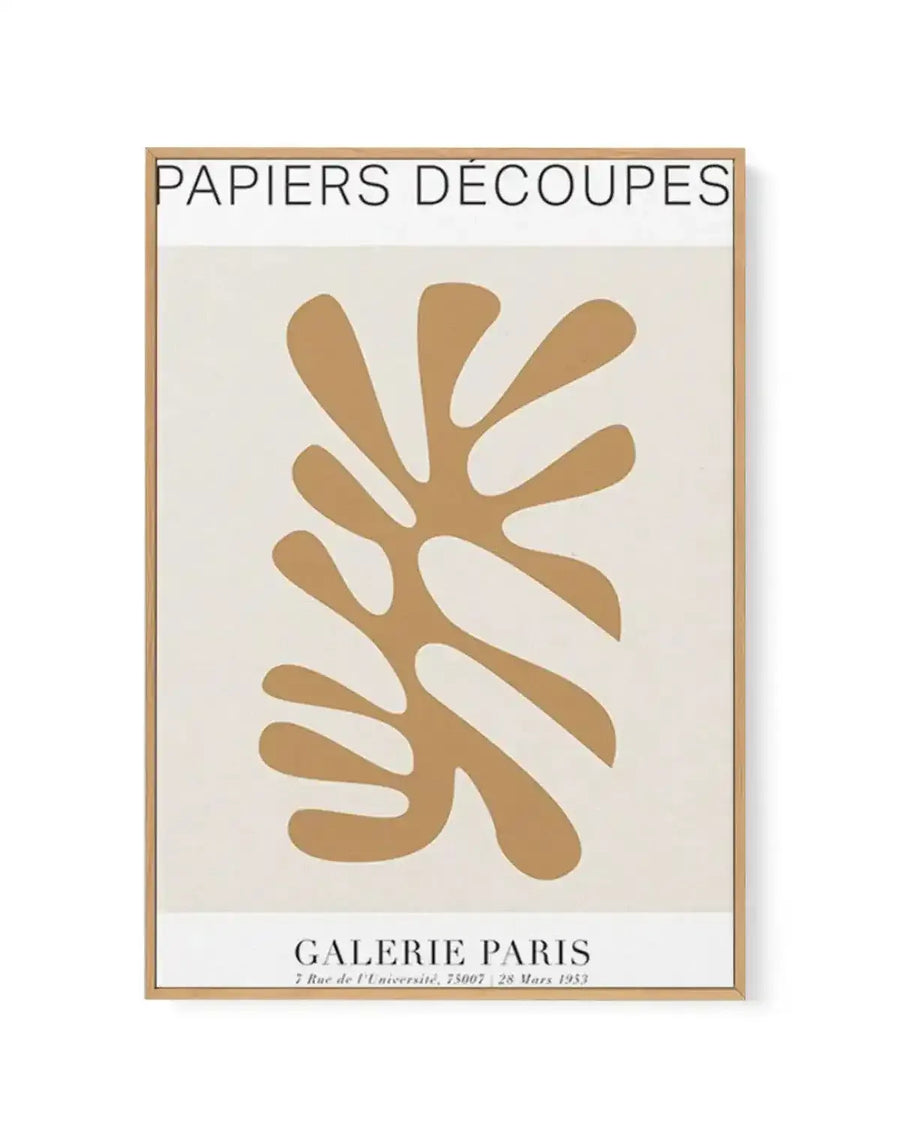 Framed art print featuring a large, abstract, organic shape in a warm, muted tan or beige colour, resembling a cut-out leaf or coral, against a soft cream background. The print includes text at the top "PAPIERS DÉCOUPES" and at the bottom "GALERIE PARIS 7 Rue de l'Université, 75007 28 Mars 1953". It is displayed in a natural wood frame with a white border.