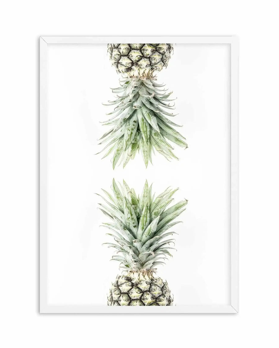 Botanical watercolor art print featuring two pineapples displayed vertically, separated by white space. The top pineapple shows a detailed golden-yellow textured fruit with an extended crown of elongated green leaves. The bottom pineapple mirrors this composition with similar detail. Rendered in soft watercolor with naturalistic shading in greens, golds, and warm earth tones. The artwork is mounted in a white frame with a white border against a clean white background.