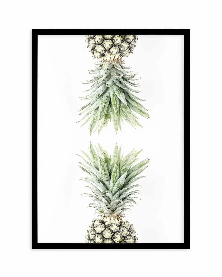 Botanical watercolor art print featuring two pineapples arranged vertically, showing detailed close-up views of the fruit's textured crown and spiky leaves in soft greens and muted yellows. The illustration uses delicate brushwork with naturalistic detail against a white background. Displayed in a black frame with white border.