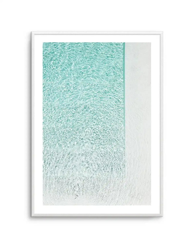 Framed photography art print capturing the shimmering surface of clear, shallow water in a swimming pool or ocean, with a bright white pool edge or sandy beach visible on the right side. The water transitions from a vibrant turquoise at the top to a lighter, almost white hue at the bottom, with ripples and reflections creating a dynamic, textured surface. The print is displayed in a white frame with a white border.
