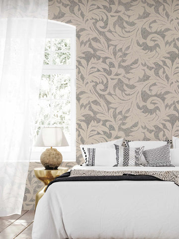 "Bedroom with a large window and sheer white curtains, featuring a wallpaper with a repeating pattern of organic, swirling leaf-like motifs in a charcoal grey stippled texture against a light beige background. A bed with white bedding, a dark grey throw, and several decorative pillows in black, white, and grey patterns is visible. A round, textured table lamp with a white shade sits on a gold side table next to the bed."