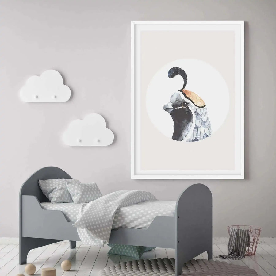 Large framed art print displayed above a grey toddler bed in a child's bedroom with light grey walls and white wooden floors. The print features a close-up watercolour illustration of a quail's head with a black and white face, brown eye, and a distinctive black feather plume, set against a light cream background with a white border and white frame. The room includes two white cloud-shaped wall hooks, a grey polka-dot duvet and pillows, a textured grey rug, and a rose gold wire basket with a striped towel.