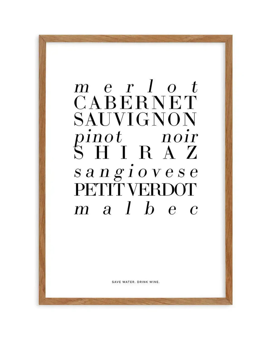 Art print in natural wood frame featuring wine variety names in varying font sizes and styles arranged vertically on white background. Text includes "merlot," "Cabernet Sauvignon," "pinot noir," "Shiraz," "sangiovese," "Petit Verdot," and "malbec" in black serif and sans-serif typefaces. Small text at bottom reads "Save water. drink wine." Light wood-grain frame with simple border.