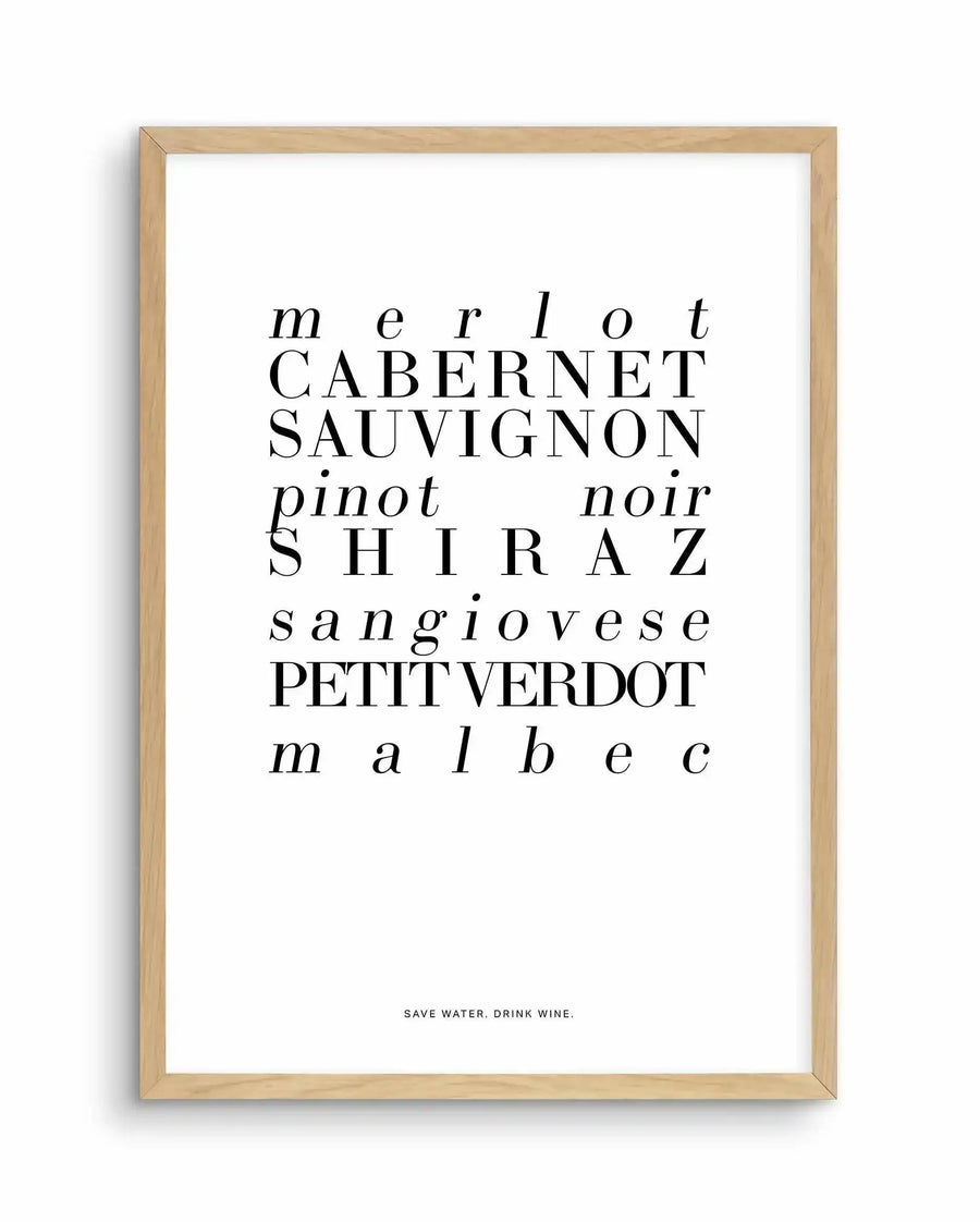 Framed art print with natural wood frame displaying white background with black typography. Text lists red wine varieties in varying font sizes and styles: "merlot," "Cabernet Sauvignon," "pinot noir," "Shiraz," "sangiovese," "Petit Verdot," and "malbec" arranged vertically. Bottom of print reads "SAVE WATER. DRINK WINE." in small capitals. Clean, minimalist design with serif and sans-serif typefaces in black ink.