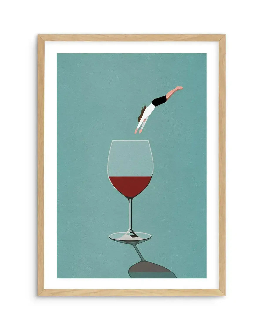 Illustration art print featuring a stylized figure diving headfirst into a large wine glass filled with red wine, set against a muted teal background, displayed in a natural oak frame with white border. The figure, wearing a white top and black shorts, is captured mid-air, with a reflection of the wine glass visible on the surface below.