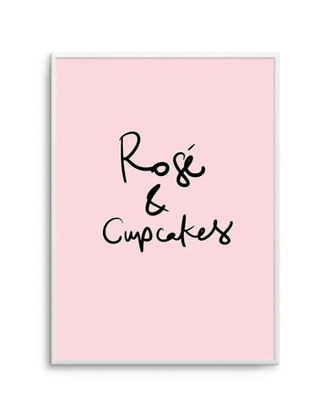 Framed art print with light pink background and black handwritten-style text reading "Rosé & Cupcakes" centered on the canvas. The text features a casual, script-like font with a small decorative dot detail. The print is mounted in a white frame with a white border.