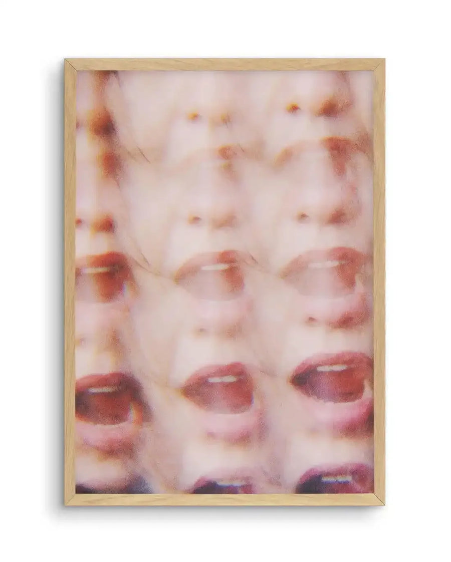Abstract art print featuring multiple blurred and overlapping images of the lower half of a face, with open mouths and eyes, in shades of pale pink, peach, and muted red, creating a sense of movement and distortion, displayed in a natural oak frame with white border.