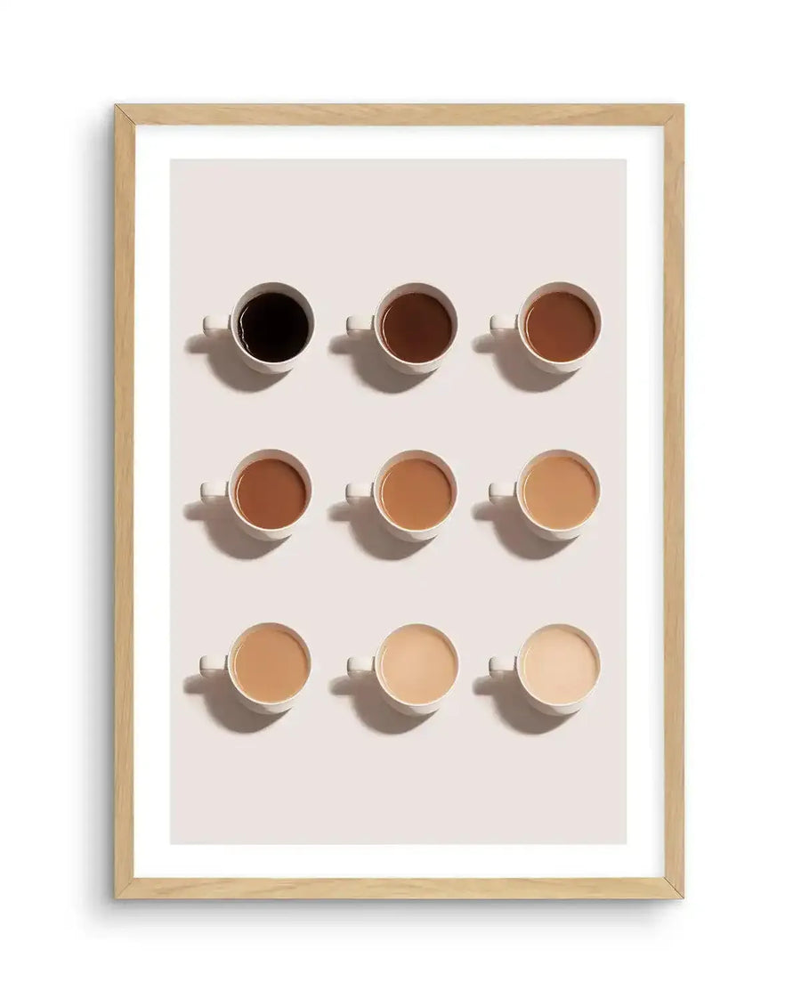 "Framed art print featuring nine coffee cups in a grid formation, each with a different shade of coffee from dark black to light cream, displayed in a natural oak frame with white border."