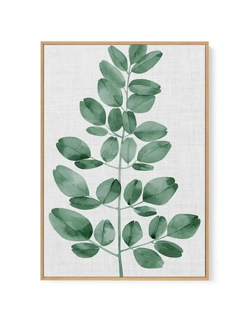 Framed canvas art print featuring a watercolor illustration of a single green botanical stem with oval-shaped leaves arranged alternately along a thin central stem. The leaves display varying shades of sage green and muted forest green with visible brushstroke texture and subtle veining details. The composition is centered vertically on a light cream linen-textured background. The artwork is set in a natural wood frame with a white border.