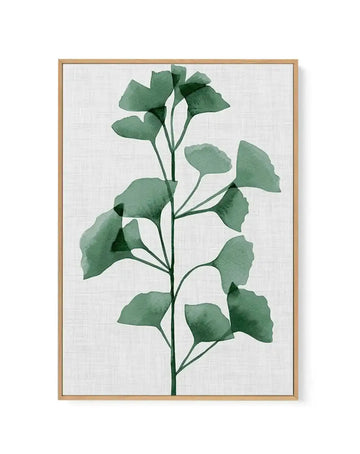 Framed canvas art print featuring a watercolor-style botanical illustration of a single green stem with multiple fan-shaped ginkgo leaves in varying shades of sage and forest green. The leaves are loosely painted with soft edges and subtle color variation, arranged along a delicate dark green stem against a white textured background. The artwork is housed in a natural wood frame with a light tan finish.