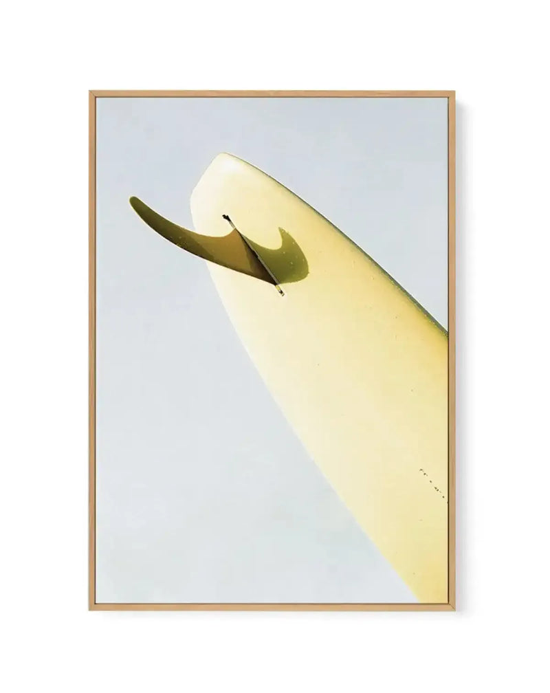 "Gallery-wrapped canvas print of a surfboard fin and tail, angled upwards against a pale blue-grey background, with a natural wood frame. The surfboard is a pale yellow-green, and the fin is a darker olive green, casting a subtle shadow. The composition highlights the sleek lines and texture of the surfboard and fin."