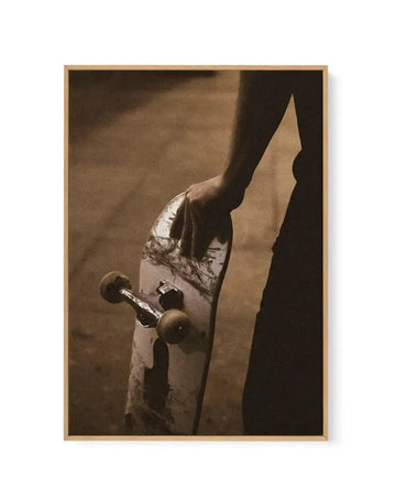 Sepia-toned photograph of a person performing a skateboarding trick against a dark background with dramatic lighting. The skateboarder wears light-colored clothing and is captured mid-motion with the skateboard visible beneath them. The image has a vintage quality with warm brown and tan tones throughout. The framed canvas print is mounted in a natural wood frame with visible depth, displaying the photograph as a gallery-style art piece suitable for wall display.