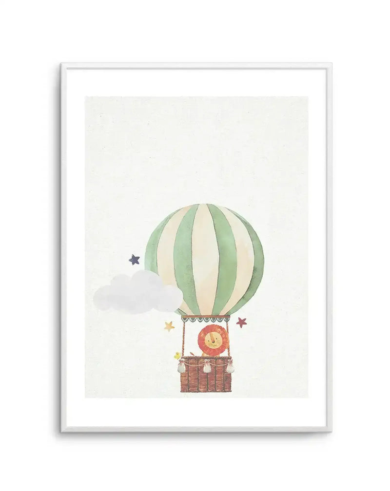 Watercolour art print featuring a hot air balloon with vertical pale green and cream stripes, carrying a smiling lion in a brown wicker basket. A white cloud and various coloured stars float around the balloon, all on a textured cream background, displayed in a white frame with a white border.