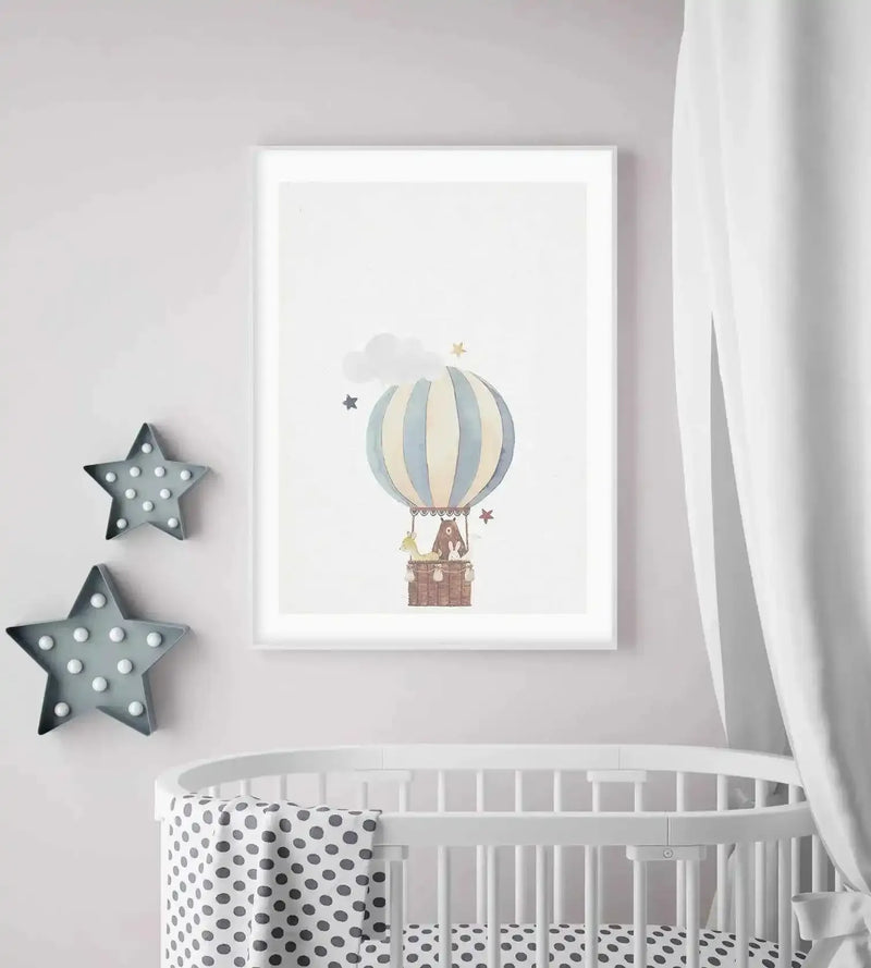 Nursery:
Framed art print displayed above a white crib in a light-toned nursery. The print features a hot air balloon illustration with vertical pale blue and cream stripes, carrying a brown bear and a rabbit in a woven basket, with small grey and gold stars and a white cloud in the background. The room includes two grey star-shaped wall lights with white bulbs and a white crib with a grey polka dot blanket.