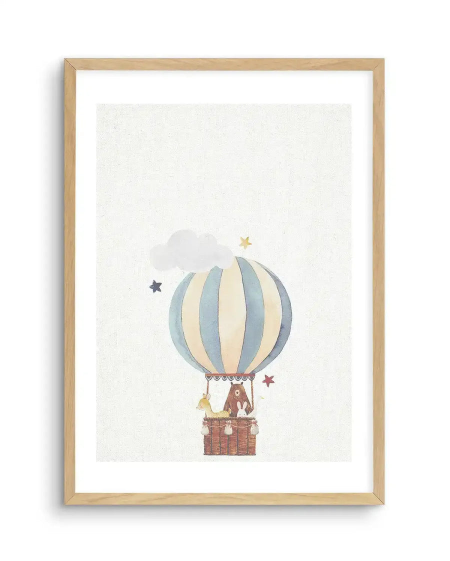 Watercolour art print featuring a hot air balloon with vertical pale blue and cream stripes, carrying a brown bear, a fawn, and a white rabbit in a woven basket. The balloon floats against a textured white background with a fluffy white cloud and scattered yellow and blue stars, displayed in a natural oak frame with white border.