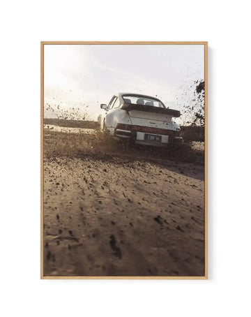"Gallery-wrapped canvas print of a white Porsche 911 driving through a muddy track, kicking up dirt and water. The car is seen from the rear, with its iconic whale tail spoiler, and the license plate reads '139 H'. The sun is low in the sky, casting a warm glow, and the overall mood is dynamic and adventurous."