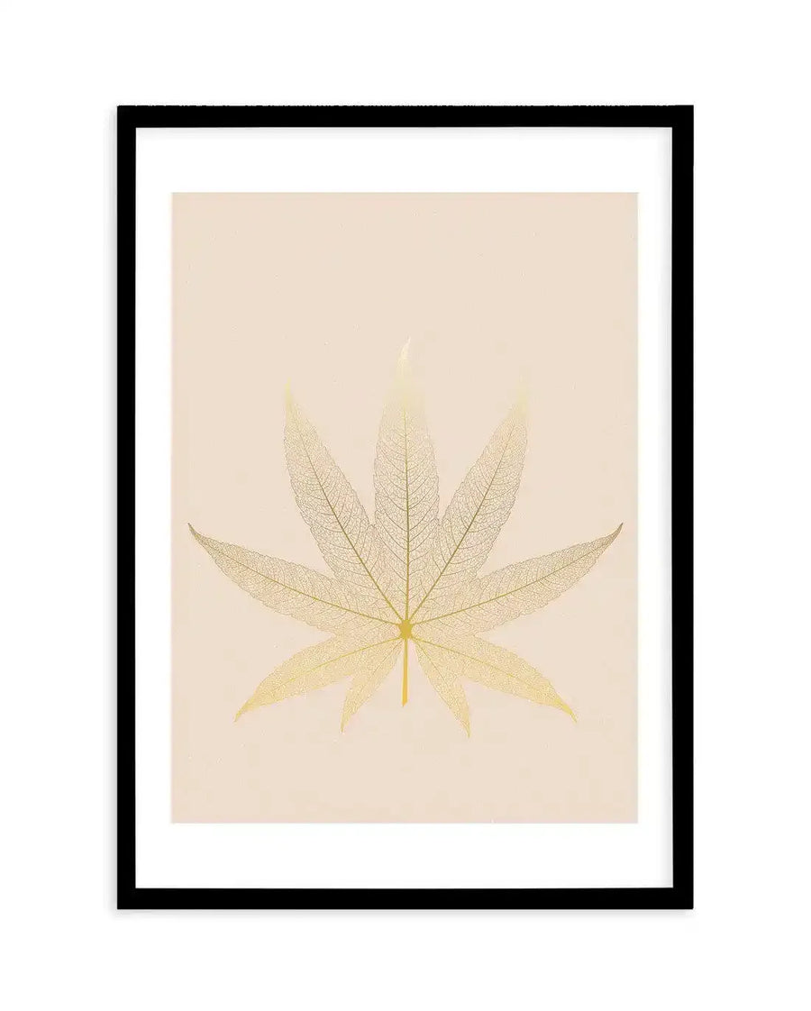 Art print featuring a delicate, skeletal leaf in a pale golden hue against a soft cream background, printed on fine art paper and displayed in a black frame with white border. The leaf is reminiscent of a cannabis or maple leaf, with seven distinct lobes, showcasing intricate vein details.