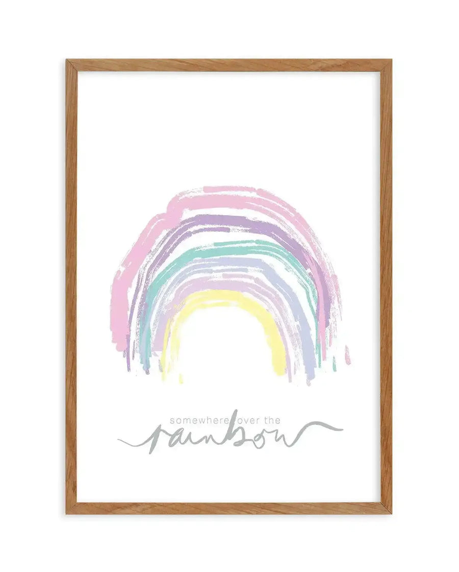 Framed art print featuring a hand-painted rainbow in soft pastels including pink, purple, lavender, mint green, and pale yellow, with brushstroke texture. Below the rainbow, gray handwritten text reads "somewhere over the rainbow." White background. Natural wood frame with visible grain texture.