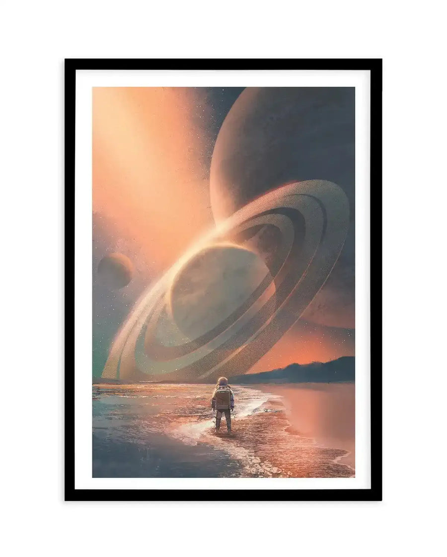 Art print featuring an astronaut standing on a reflective shore, gazing at a celestial landscape with multiple planets and prominent rings, under a sky with warm orange and cool blue hues, displayed in a black frame with a white border.