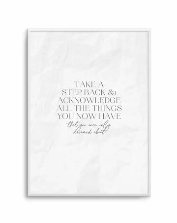 "Motivational art print featuring the quote 'TAKE A STEP BACK & ACKNOWLEDGE ALL THE THINGS YOU NOW HAVE that you once only dreamed about' in black serif and script fonts on a textured white background, displayed in a thin white frame with a white border."