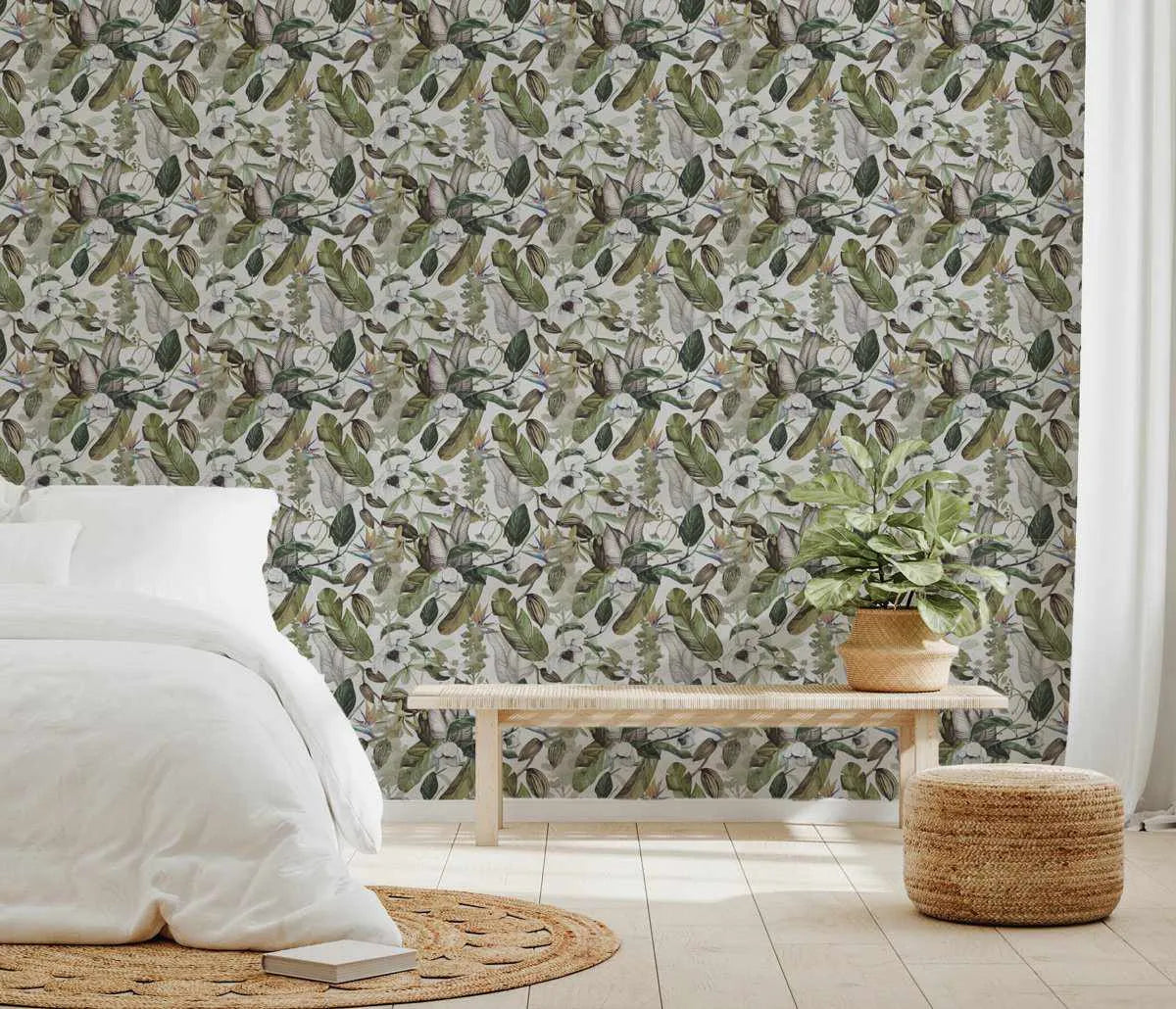 Tathra Wallpaper displayed on a bedroom wall featuring a dense botanical illustration pattern. The design shows a repeating composition of sage green, olive, and cream-colored leaves, flowering branches, and delicate botanical elements in a painterly style against a light neutral background. The wallpaper is shown in a serene bedroom setting with a white bed, natural wood bench, woven storage baskets, and neutral flooring, creating a calm, nature-inspired interior aesthetic.