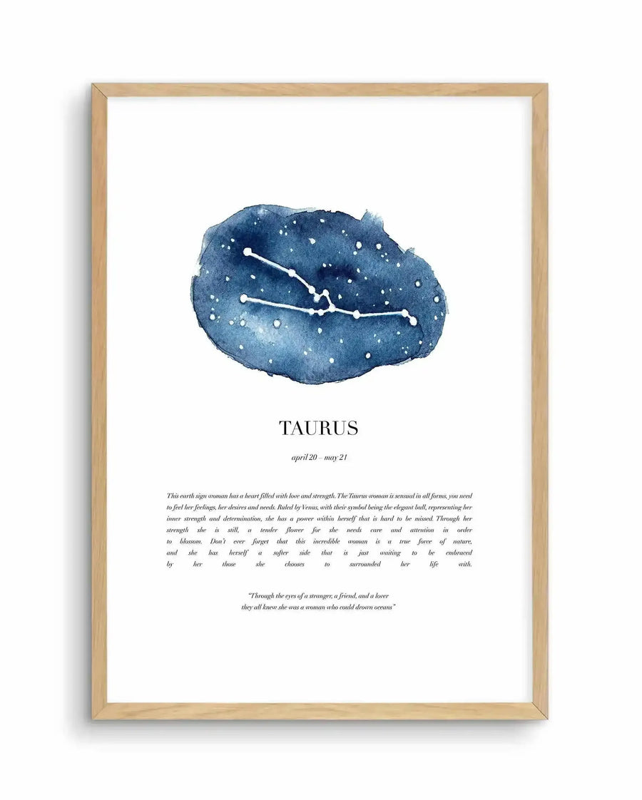 Watercolour art print featuring the Taurus zodiac constellation in white stars and lines on a deep blue, cloud-like background with white speckles, displayed in a natural oak frame with white border. Below the constellation, the word "TAURUS" is printed in black, followed by "april 20 - may 21" in a smaller font. Further below, a paragraph describes the Taurus woman, and a quote is printed at the bottom.