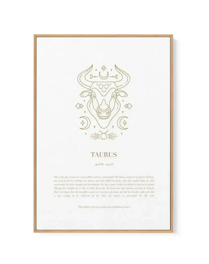 Framed canvas print featuring a minimalist gold line art illustration of a Taurus bull's head, surrounded by celestial elements like crescent moons and stars, on a clean white background. Below the illustration, the word "TAURUS" is written in a bold serif font, followed by "april 20 - may 21" in a smaller, lighter font. Further down, a paragraph of text describes the Taurus zodiac sign. The canvas is displayed in a natural wood frame.