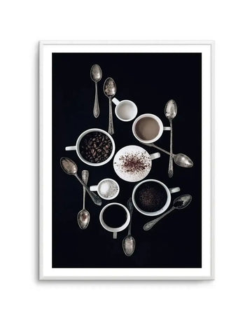 Framed photography art print on a black background, featuring various white ceramic cups and antique silver spoons arranged in a circular composition. The cups contain coffee beans, ground coffee, a frothy coffee drink with chocolate sprinkles, and a light brown coffee drink.