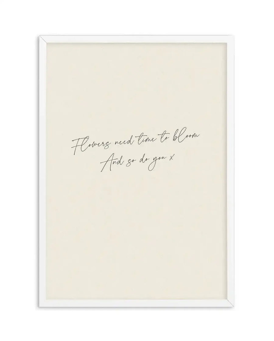 Art print featuring the handwritten quote "Flowers need time to bloom And so do you x" in black script on a warm cream background, displayed in a white frame with white border.