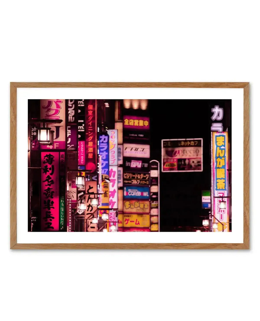 Framed photography art print capturing a vibrant night scene in Tokyo's Red Light District, featuring numerous neon signs in various shades of pink, red, blue, and yellow against a dark background, with a natural oak frame and white border. The signs display Japanese characters, advertising businesses like karaoke, internet cafes, and games, creating a bustling, energetic atmosphere.