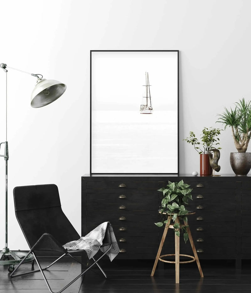 Trawlor art print in black frame, leaning on dark wood drawers styled with leather chair and trailing plants